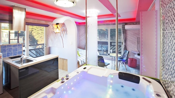 Un baño moderno con una bañera grande, un lavamanos y una zona de ducha. Se ve un balcón con muebles de exterior a través de las puertas de cristal.