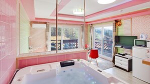 Un baño moderno con una bañera grande, zona de ducha y tocador con espejo. Hay una ventana que ofrece vistas al exterior.