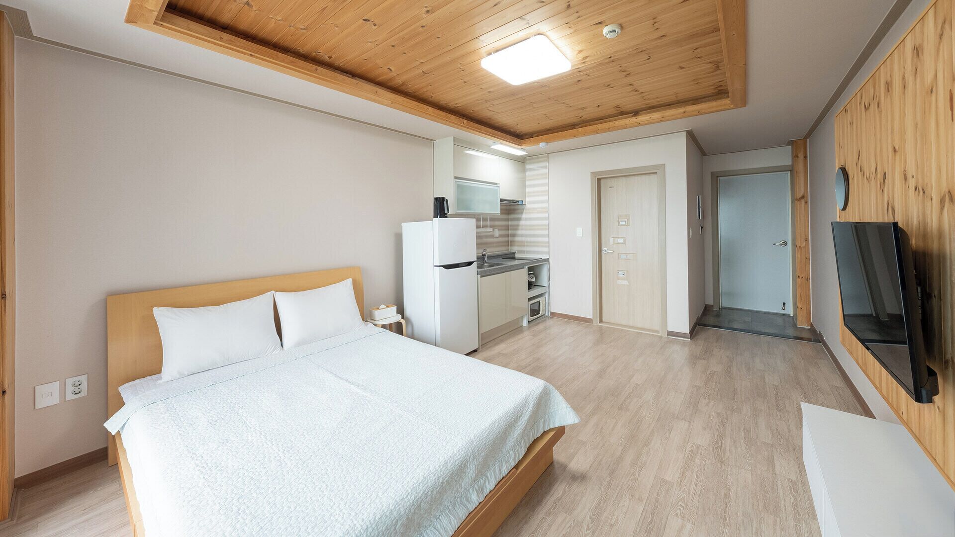 Un dormitorio con cama, kitchenette y televisión montada en la pared.