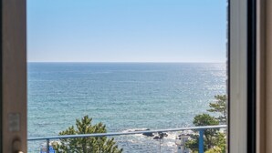 Vista do mar através de uma janela, com um corrimão e alguma vegetação ao primeiro plano.