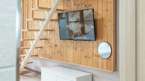 Um interior moderno com uma parede de madeira, uma TV fixada nela, um espelho redondo e um armário branco.