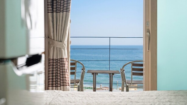 Uma varanda com vista para o mar, uma mesa e duas cadeiras.