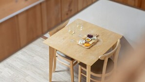 Uma mesa de madeira com toalha branca, duas taças de vinho e um prato de queijos com uvas e biscoitos.