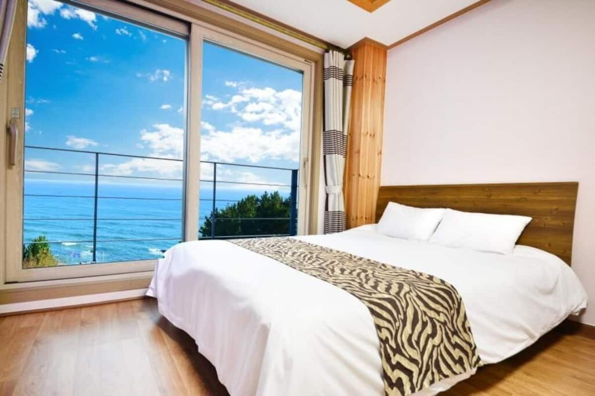 Une chambre avec une grande fenêtre, un lit et une vue sur l’océan.