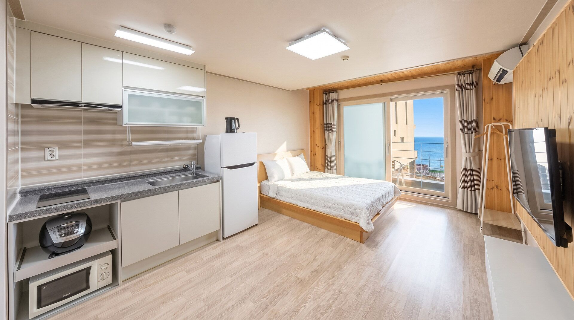 A compact room with a kitchenette, a bed, and a balcony with a view.