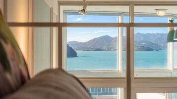 A room with a large window offering a view of a body of water and mountains.