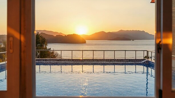 Una piscina infinita con vistas al océano y a las montañas al atardecer.