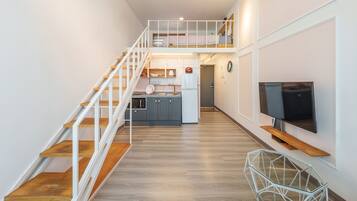 A modern apartment with a wooden staircase, a kitchen with a white refrigerator, and a flat-screen TV mounted on the wall.