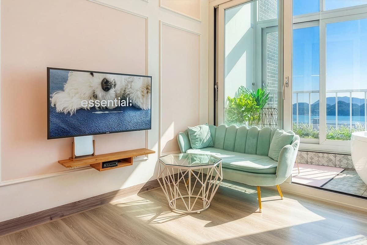 Ett modernt vardagsrum med en tv, en ljusgrön soffa, ett soffbord i glas och utsikt över havet genom stora fönster.