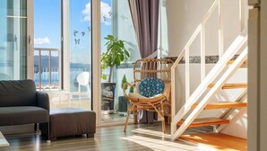 Una sala moderna con un sofá, un sillón de mimbre, una escalera y ventanas grandes.