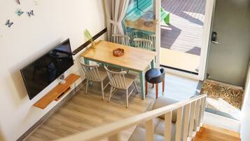 Un comedor con una mesa y sillas de madera, un televisor sobre un mueble bajo, y vista a la terraza exterior a través de un ventanal.