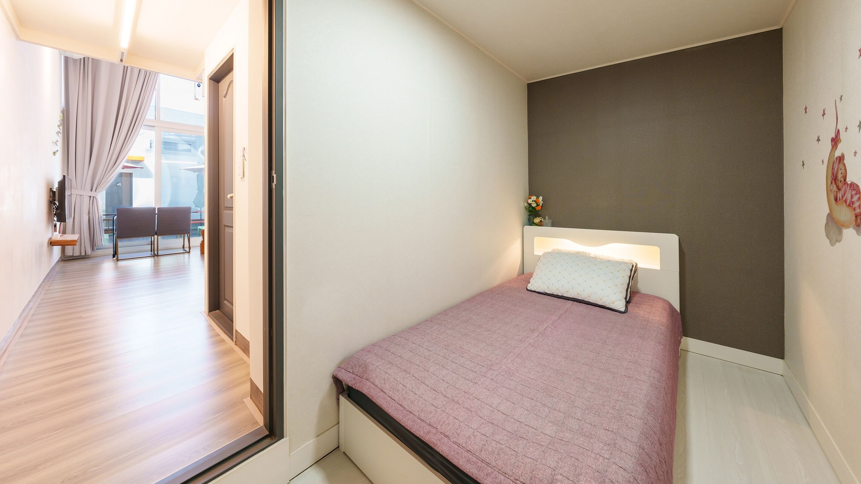 Ein Schlafzimmer mit Bett, Nachttisch, einem Fenster mit Vorhängen und Blick ins Freie.