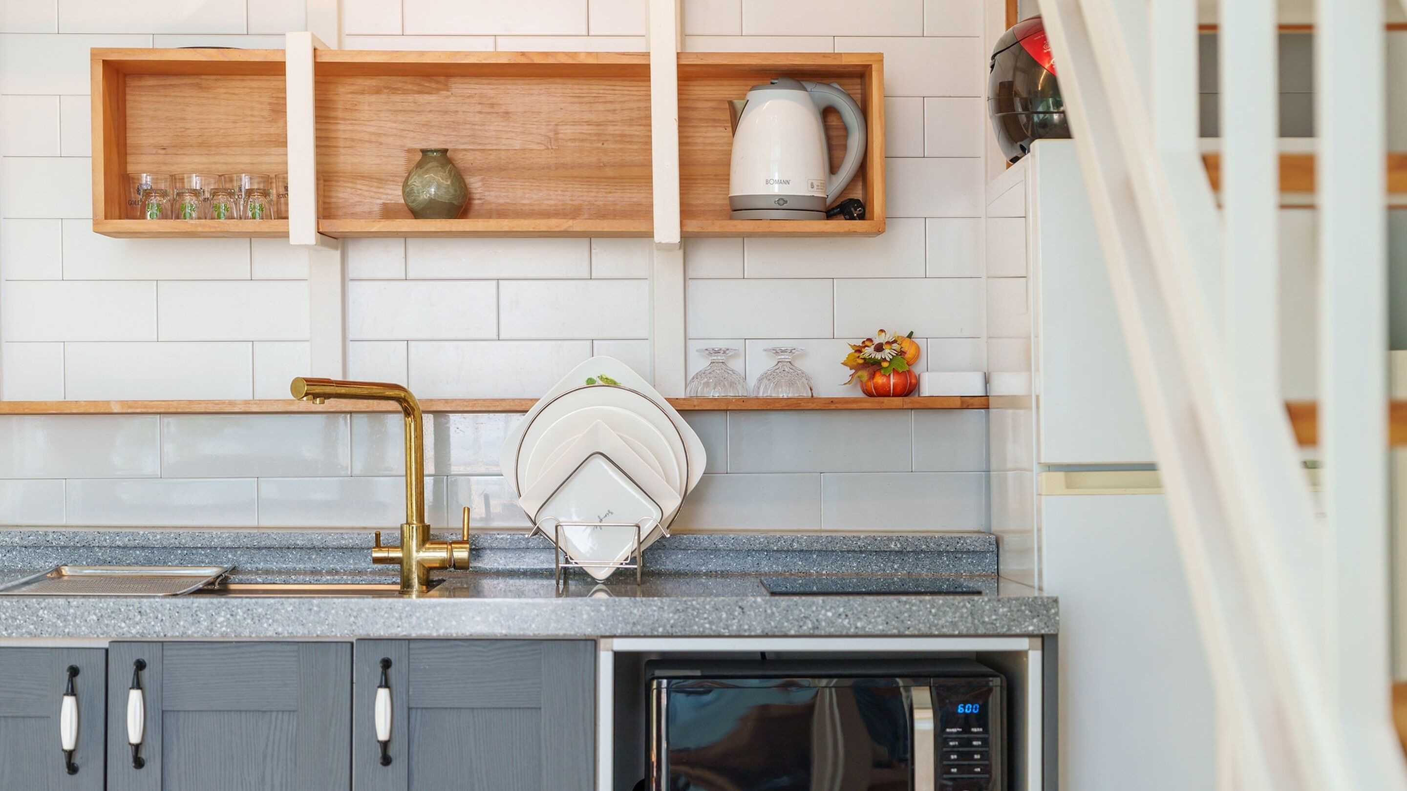 A kitchen with a modern design, featuring a stainless steel sink, a microwave, and wooden shelves above the counter.
