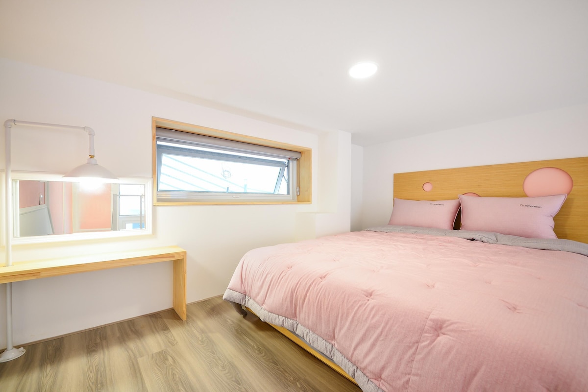 A bedroom with a bed, a desk, a window, and a ceiling light.