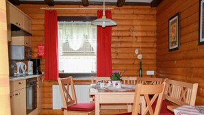 L’intérieur d’un chalet en bois comprend une table à manger, des chaises, un coin cuisine et une fenêtre avec des rideaux.