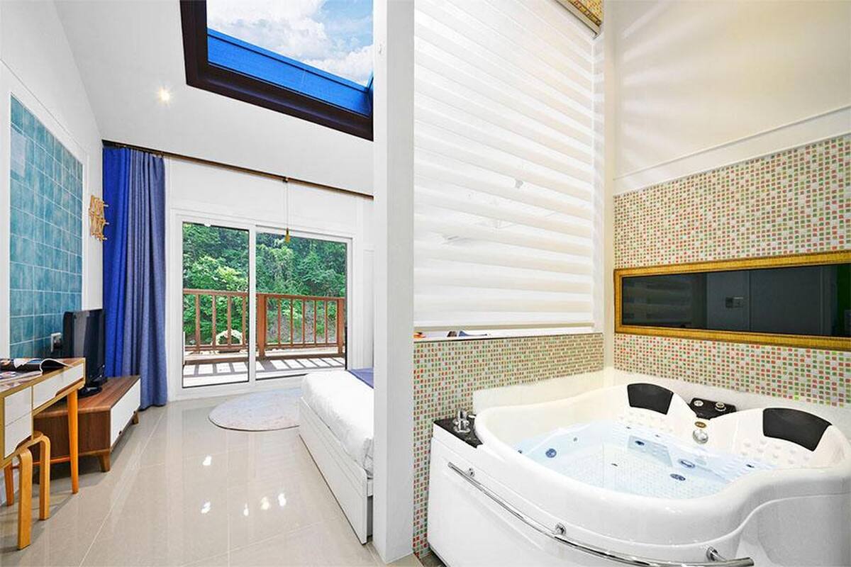 A modern bathroom with a large bathtub, a shower area, and a balcony with a view of greenery.