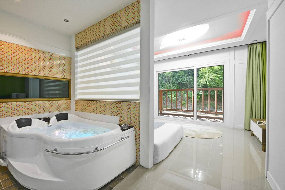 A modern bathroom with a large bathtub, a mirror, and a view of a balcony with greenery.