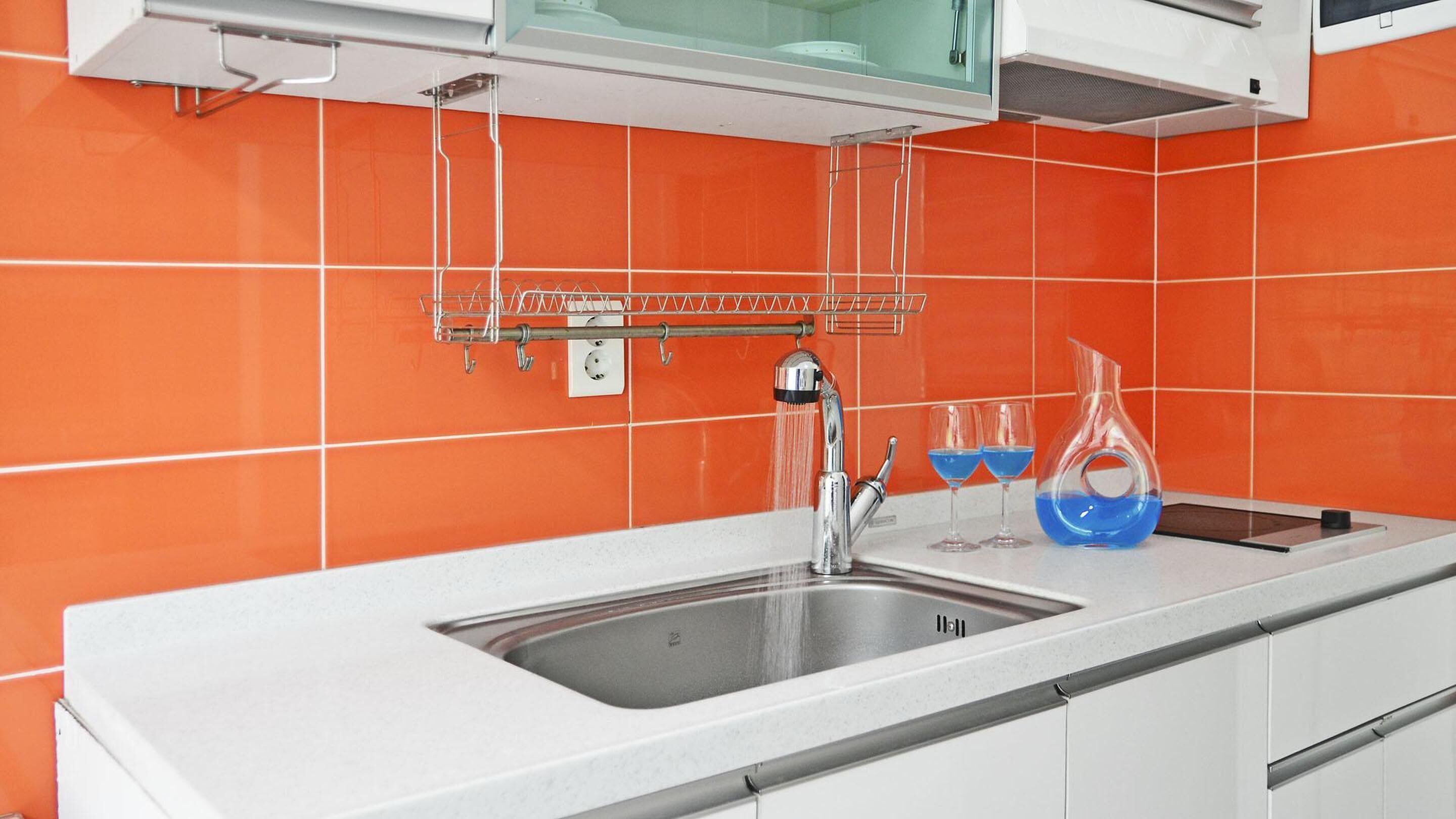 Une cuisine dotée d’un évier en acier inoxydable, d’un robinet et d’un pare-éclaboussures recouvert de carreaux orange.