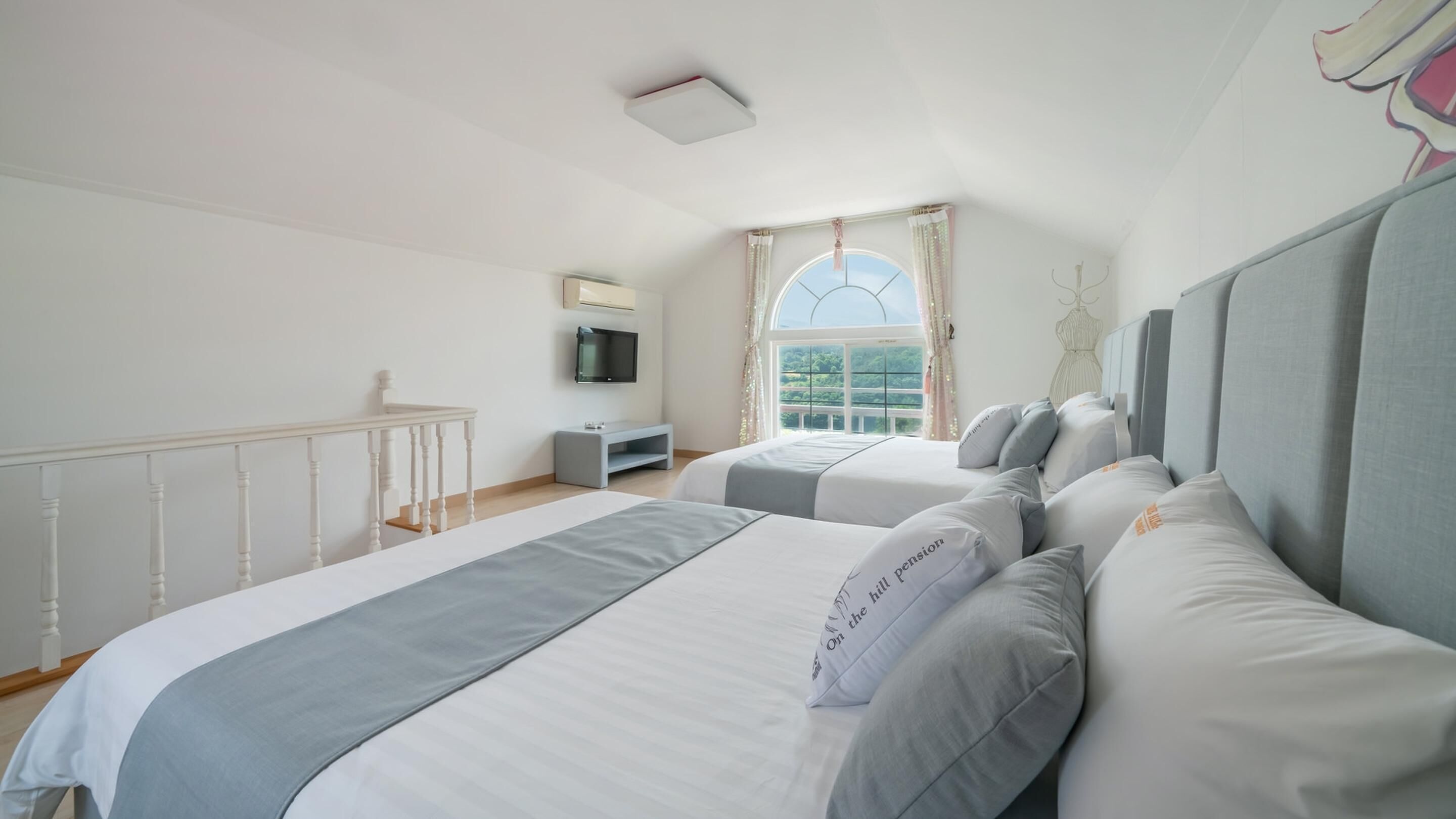 A bedroom with two beds, a TV, a window with curtains, and a balcony railing.