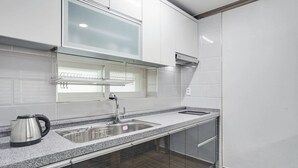 Una cocina moderna con armarios blancos, un lavamanos de acero inoxidable, un hervidor y una ventana sobre el lavamanos.