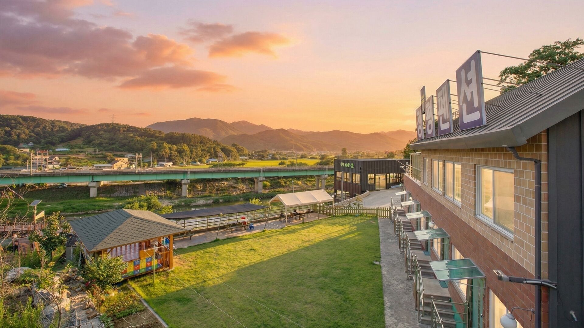 Un hôtel offrant une vue sur une rivière et des montagnes, doté d’un espace extérieur couvert aménagé en salon et d’un bâtiment moderne avec de grandes fenêtres.