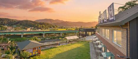 Un hotel con vistas a un río y montañas, un área de estar al aire libre techada y un edificio moderno con grandes ventanales.