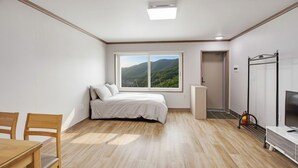 Un dormitorio con una cama, una ventana con vista a la montaña, un televisor y un escritorio con una silla.