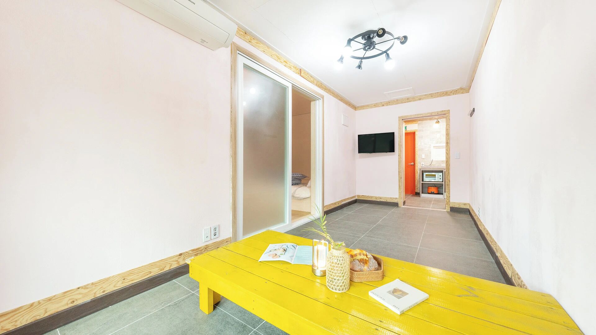 A hallway with a yellow bench, a television mounted on the wall, and a ceiling fan.
