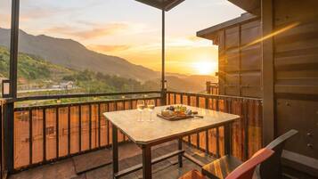 A balcony with a table set for two, a chair, and a scenic mountain view at sunset.