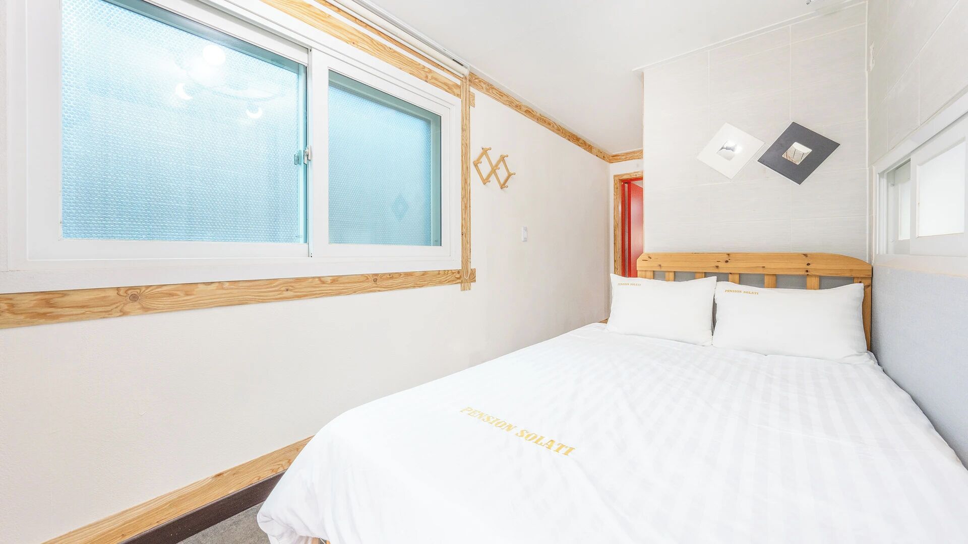 Un dormitorio con cama, ventana y lámpara en la pared.