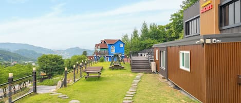 A residential area with a blue house, a wooden building with a sign, and a stone pathway leading to a wooden deck.