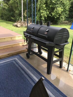 A black barbecue grill with wheels, a gas tank, and a control panel.