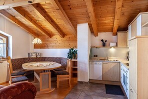 Una cocina acogedora con vigas de madera, una zona de comedor con una mesa redonda y sillas, además de un banco empotrado.