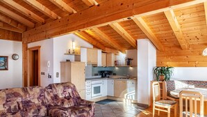 A cozy living room with a sofa, wooden dining table, chairs, and a kitchen area with cabinets and appliances. - Apartment "Ahornblick" with Mountain View, Wi-Fi & Balcony (Gattererberg)