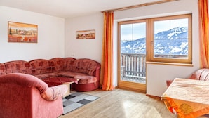 A living room with a sofa, a bed, a window with a view of mountains, and two paintings on the wall.