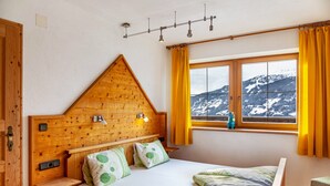 A room with a wooden headboard, a bed with green and white bedding, a window with a mountain view, and a wooden nightstand.