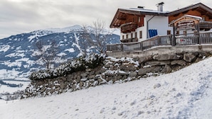 A chalet with a stone wall, wooden balcony, and a sign indicating it is a guesthouse.