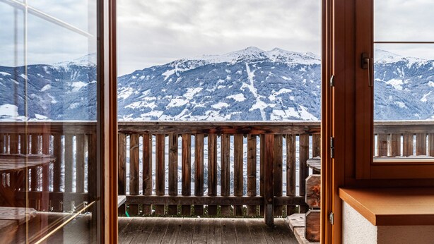 A balcony with a wooden railing overlooking a snowy mountain landscape.