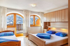 Un dormitorio con dos camas, cabeceros de madera, un balcón con vistas a montañas nevadas y un ventanal con cortinas.