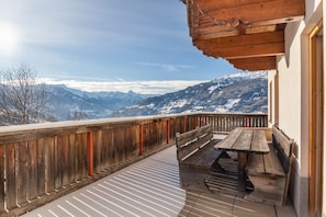 A balcony with a wooden bench and table, overlooking a mountainous landscape.