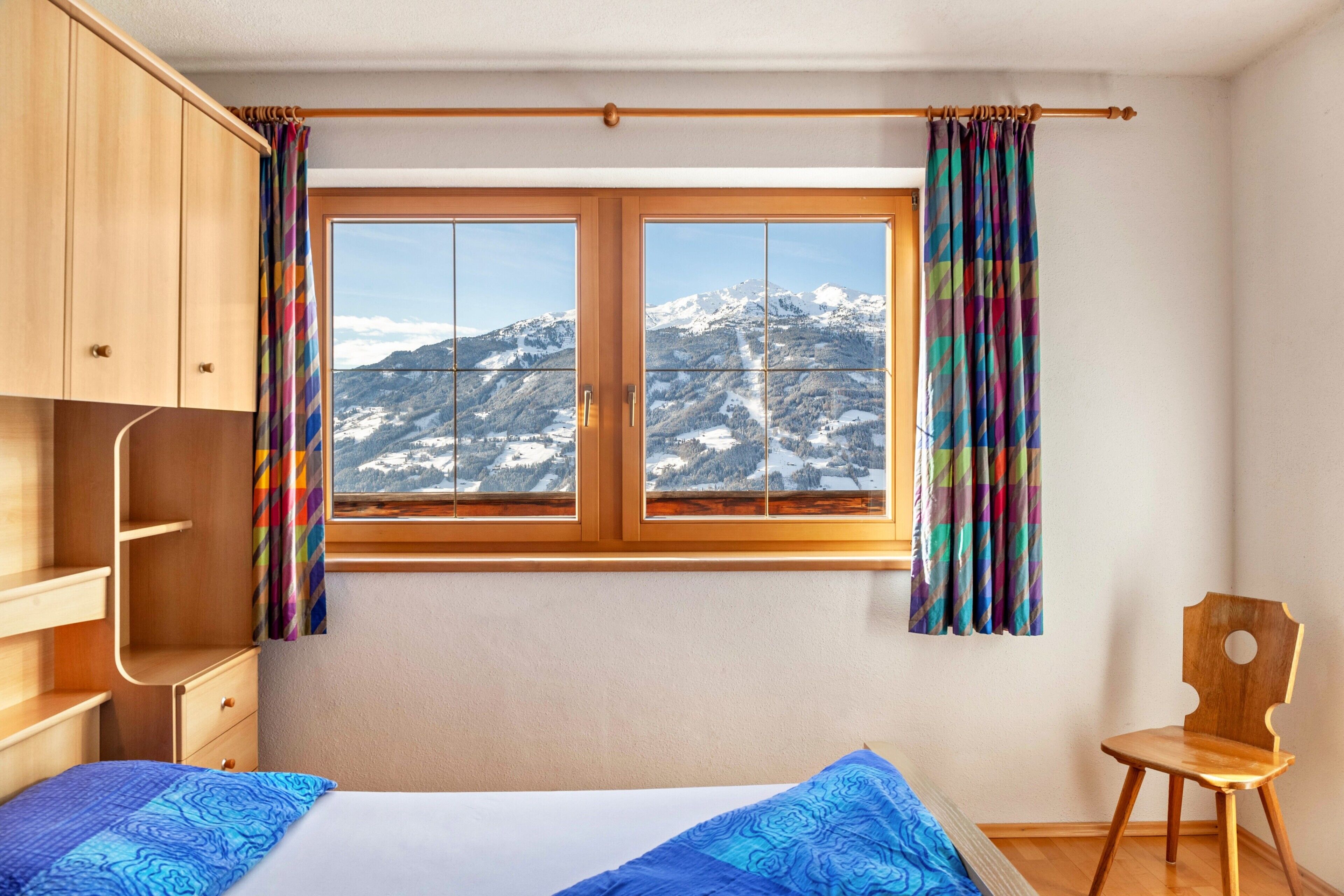 Ein Schlafzimmer mit Bett, Holzschrank, Stuhl und Fenster mit Bergblick.