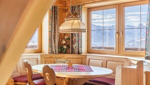 A cozy dining area with a round table, wooden chairs, and a bench, featuring a mountain view through large windows. - Apartment "Zillertal 3000" with Mountain View, Wi-Fi & Terrace (Gattererberbg)