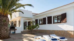 Una villa con patio de piedra, mobiliario exterior, horno para pizza y piscina.