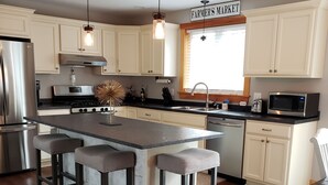 A kitchen with white cabinets, a central island with stools, stainless steel appliances, and a sign reading "FARMER'S MARKET". - If you want privacy, look no further! (Arundel)