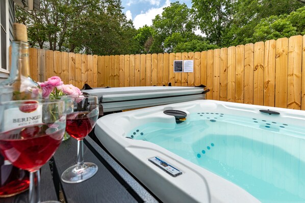 Un bain à remous avec une clôture en bois en arrière-plan, une bouteille de vin et deux verres à vin posés sur une table.