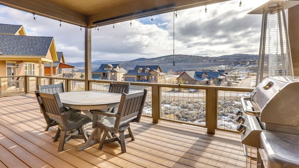 Une terrasse en bois avec une table et des chaises, d’où l’on a vue sur un quartier résidentiel avec ses maisons et, au loin, sur une chaîne de montagnes.