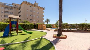 A playground with a slide and climbing structure, surrounded by a well-maintained lawn and a palm tree.