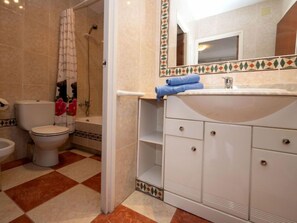 A bathroom with a toilet, bidet, and shower. There is a sink with a mirror above it and a towel on the counter.
