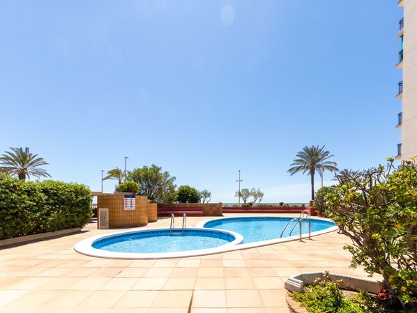 A rooftop swimming pool area with two pools, surrounded by palm trees and a clear blue sky.