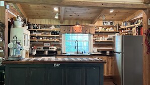 A spacious kitchen with wooden beams, a central island, and a pantry area. - Natchez Hideaway ~ Rustic Cabin on 50 acres outside Nashville near Leipers Fork (Franklin)